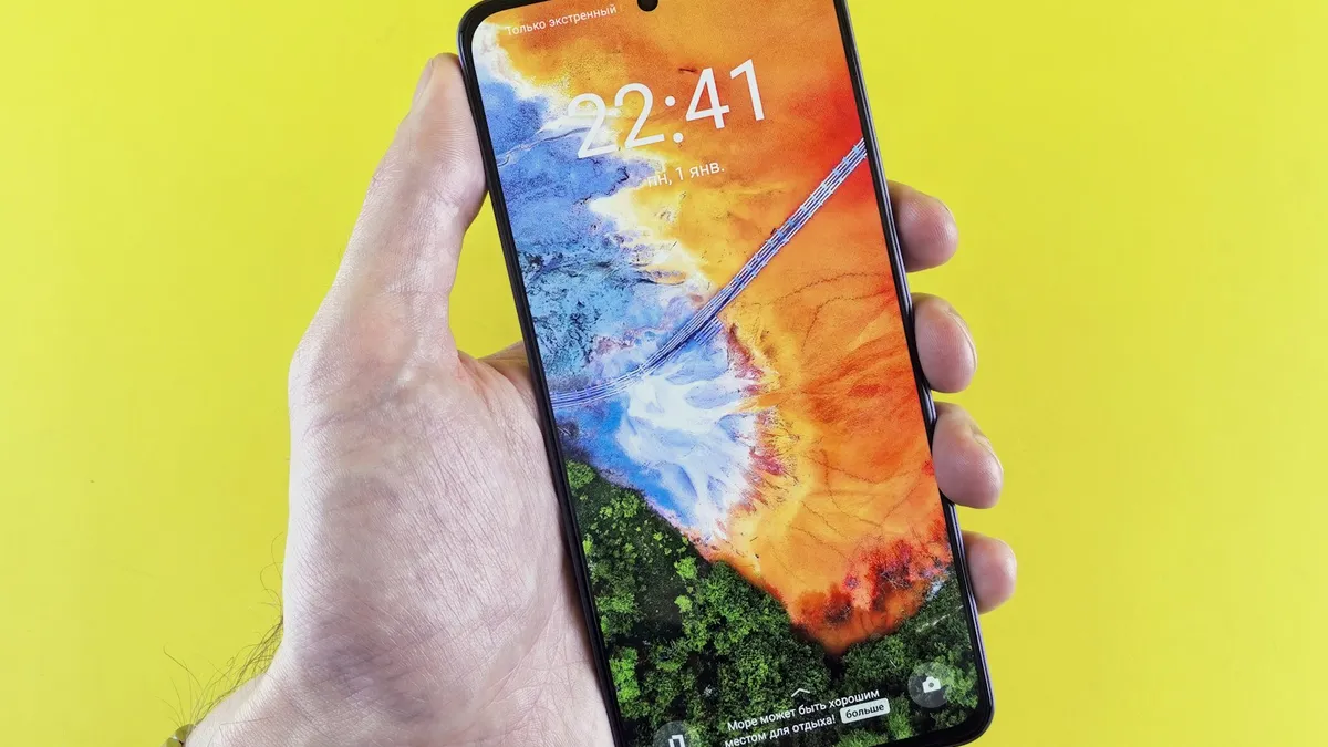 A hand holding an Android phone with the lock screen showing the time against a yellow background